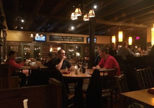 A cozy restaurant interior with wooden decor, dim lighting, and patrons dining at tables.