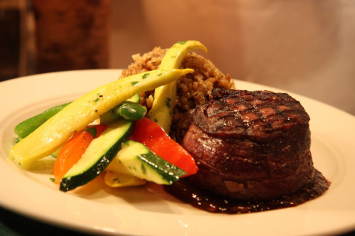 A plated meal featuring a grilled steak, colorful sautéed vegetables, and a serving of rice.