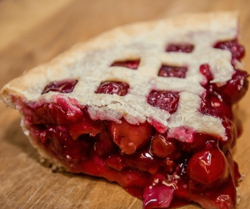 A slice of cherry pie with a lattice crust, resting on a wooden surface.