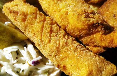 Close-up of crispy, golden-brown fried fish fillets served with coleslaw and pickles.