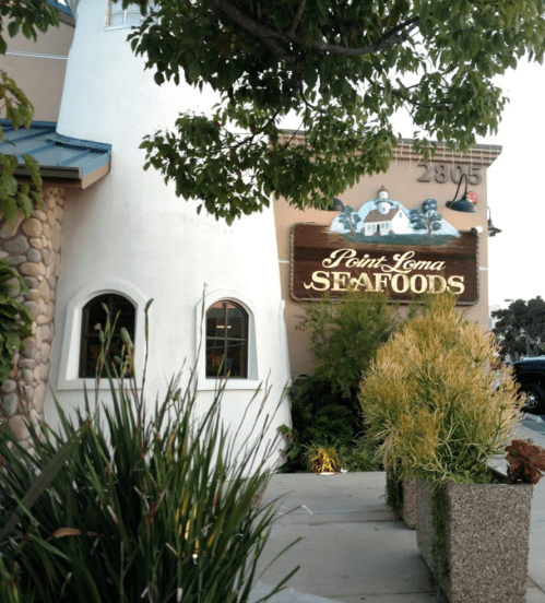 Sign for Point Loma Seafoods on a building, surrounded by greenery and a clear sky.