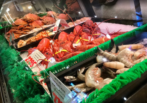 A seafood display featuring crabs, lobsters, and shrimp on ice with price tags.