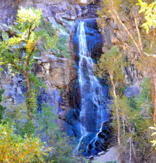 A serene waterfall cascading down rocky cliffs, surrounded by lush green trees and vibrant foliage.