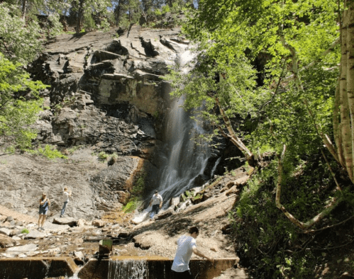A scenic waterfall cascades down rocky terrain, with people enjoying the natural surroundings and splashing in the water.