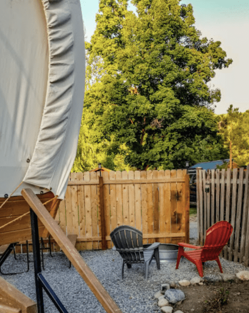 A cozy outdoor space with two chairs, a fire pit, and a wooden fence surrounded by greenery.