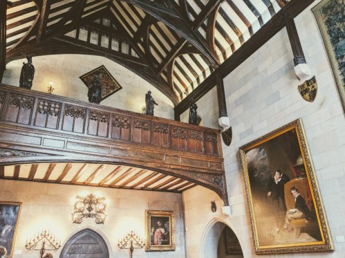 Interior of a grand hall featuring wooden beams, ornate paintings, and statues on a balcony.