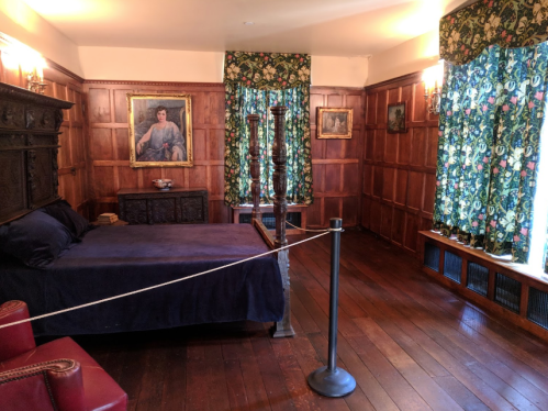 A cozy bedroom with wooden paneling, a dark bed, floral curtains, and vintage artwork on the walls.