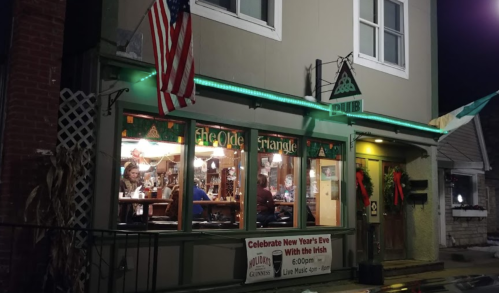 A cozy pub at night, decorated for the holidays, with people inside and an American flag outside.