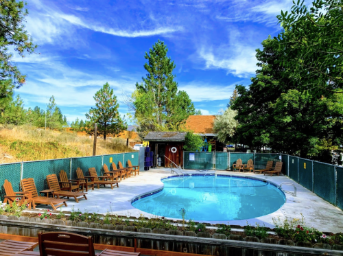 A serene pool area surrounded by trees, with wooden lounge chairs and a clear blue sky above.