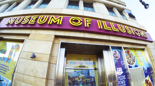 Exterior view of the Museum of Illusions, featuring a colorful sign and promotional posters for upcoming art exhibits.