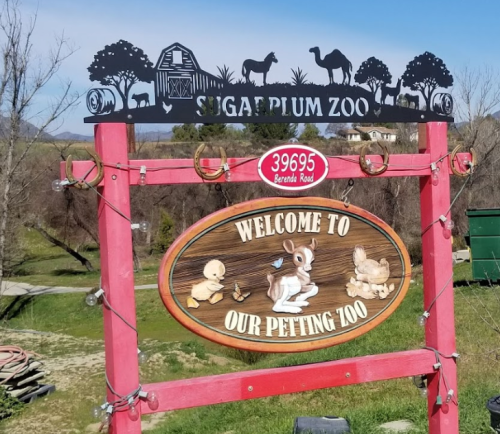 Sign for Sugar Plum Zoo featuring a petting zoo welcome, with decorative animals and a scenic background.