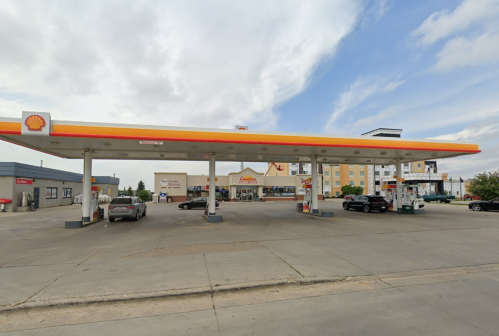 A Shell gas station with a convenience store and cars at the pumps under a cloudy sky.