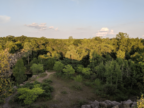 A scenic view of a lush green landscape with trees and a rocky cliff under a clear blue sky.