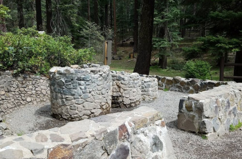 Stone structures in a forested area, surrounded by trees and gravel pathways.