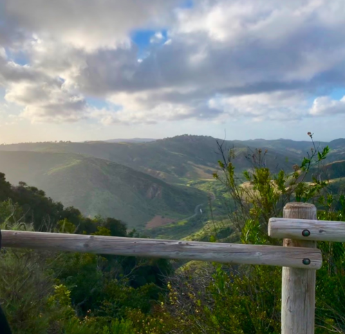 Scenic view of rolling hills and valleys under a cloudy sky, framed by a wooden railing.