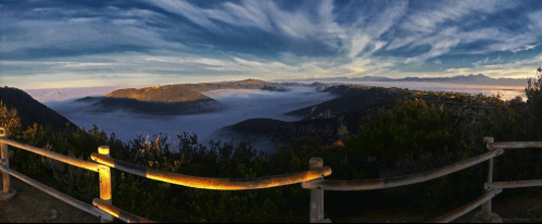 A panoramic view of misty hills under a colorful sky, framed by a wooden fence.