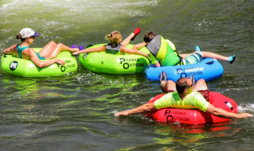 Four people float on colorful inner tubes in a river, enjoying a sunny day outdoors.