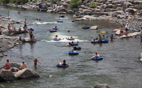 People floating on inner tubes and swimming in a river surrounded by rocks on a sunny day.