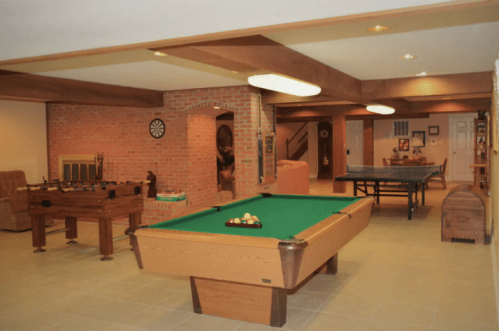 A spacious game room featuring a pool table, foosball table, ping pong table, and cozy seating area.