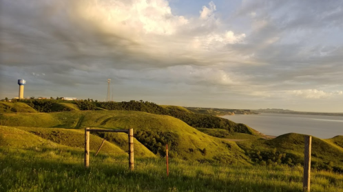 A scenic view of rolling green hills under a cloudy sky, with a river and distant land in the background.