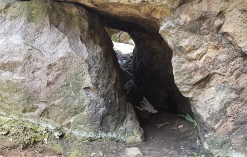 A narrow passageway between large rocks, leading into a dark cave-like space. Green moss is visible on the ground.