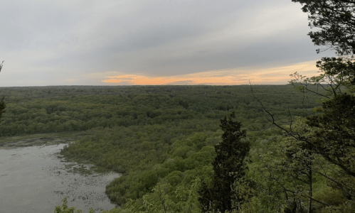 A scenic view of a lush green landscape with a calm lake and a sunset sky in the background.