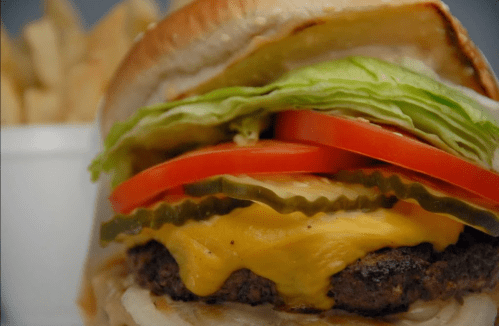 Close-up of a cheeseburger with lettuce, tomato, and pickles, served with a side of fries.