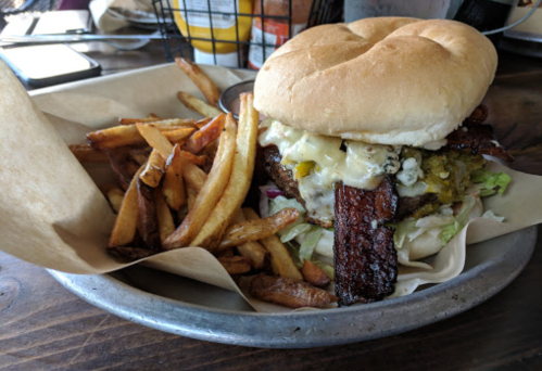 A juicy burger with bacon, cheese, and toppings, served with a side of crispy fries on a metal plate.