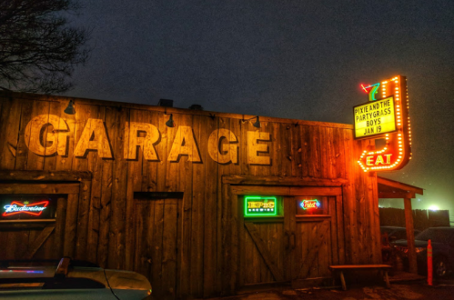 A rustic garage building with a neon sign advertising a music event, illuminated at night.