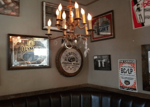 A cozy bar corner featuring a chandelier, vintage signs, and a wooden barrel on the wall.