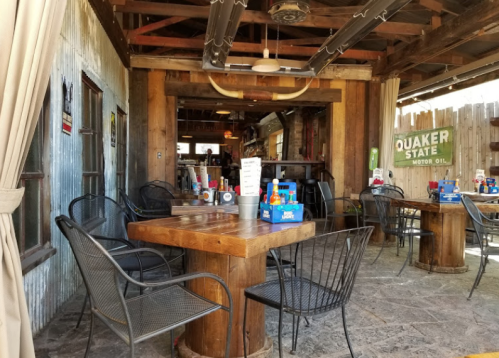 Rustic dining area with wooden tables, black chairs, and a vintage decor featuring metal walls and signage.