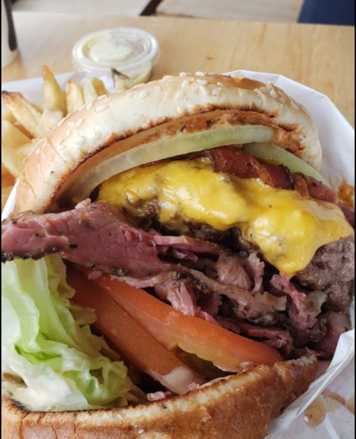 A close-up of a loaded burger with layers of meat, cheese, lettuce, and tomato, served with fries on the side.