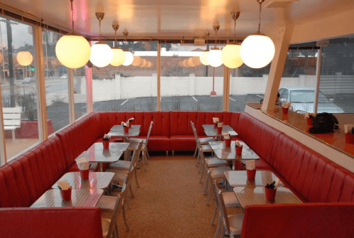 A retro diner interior with red booths, metal tables, and round pendant lights, creating a cozy atmosphere.