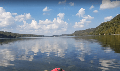 A serene lake scene with calm waters reflecting fluffy clouds and green hills under a blue sky.