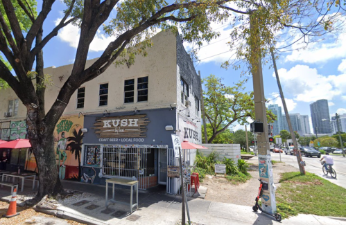 A corner restaurant named "KUSH" with outdoor seating, surrounded by trees and city buildings in the background.