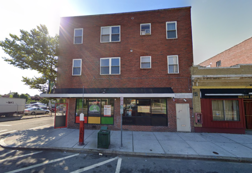 A brick building with multiple windows, a storefront, and a tree nearby, located on a city street.