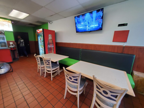 Interior of a casual dining area with tables, chairs, a Coca-Cola fridge, and a TV displaying a performance.