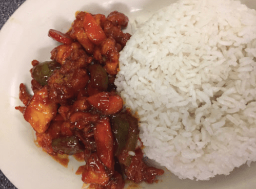 A plate of fried chicken in a spicy sauce with bell peppers, served alongside a mound of white rice.