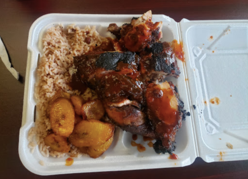 A takeout container with grilled chicken, rice, and fried plantains, drizzled with sauce.