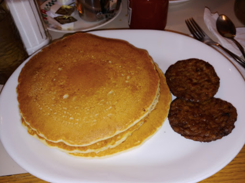 A plate with three fluffy pancakes and two sausage patties, served on a white dish.