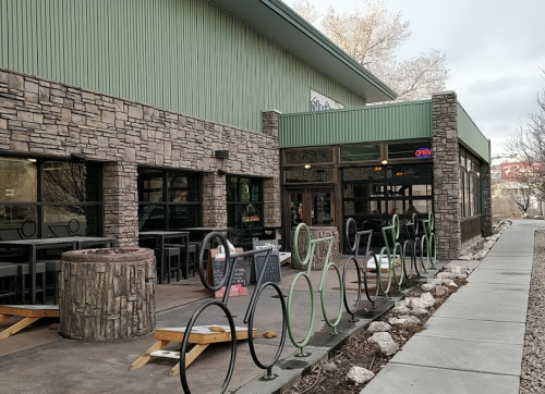 Exterior of a restaurant with stone walls, large windows, and a bike rack in front, featuring an "Open" sign.