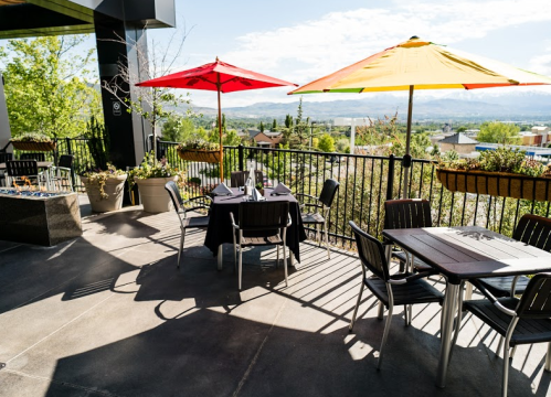 A sunny outdoor dining area with colorful umbrellas, tables, and scenic views of greenery and mountains.