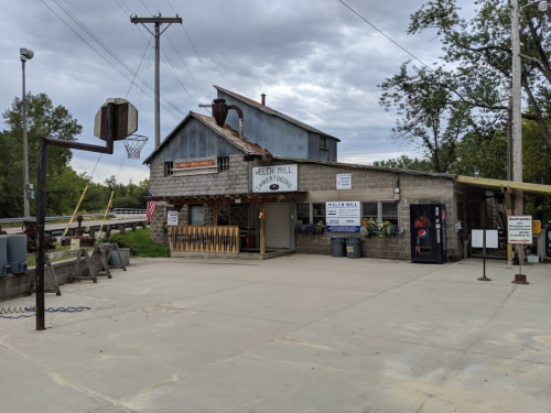 A rustic building labeled "Welch Mill" with a basketball hoop, surrounded by trees and power lines.