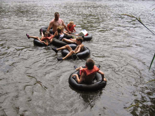 A group of children and an adult float on inner tubes in a river, enjoying a sunny day outdoors.