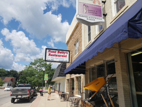 Aunt Betty's Restaurant and a dance studio sign on a sunny street, with a person walking by.