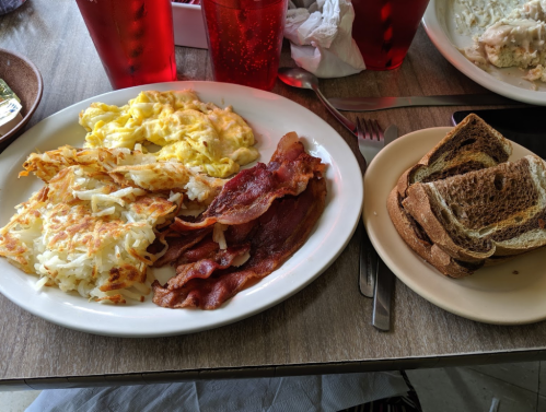 A plate of scrambled eggs, crispy bacon, hash browns, and a side of toasted bread on a table.