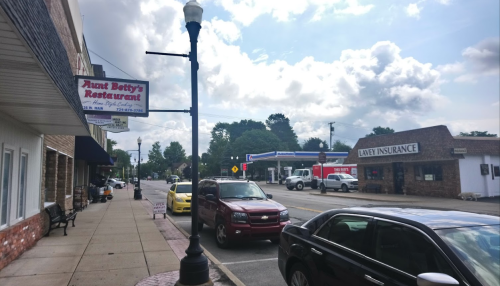A street view featuring Aunt Betty's Restaurant, parked cars, and nearby businesses under a cloudy sky.