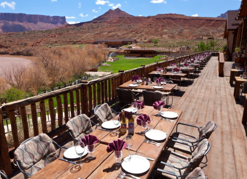 Outdoor dining area with tables set for a meal, overlooking a scenic landscape of mountains and a river.