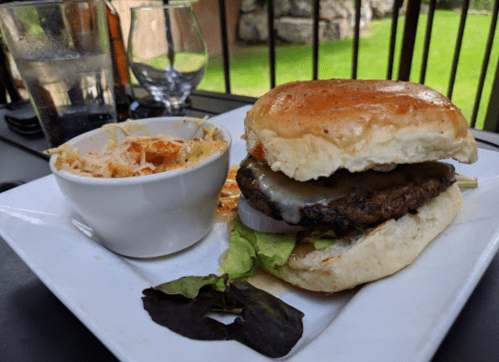 A juicy burger with lettuce, onion, and melted cheese, served with a side of coleslaw on a white plate.