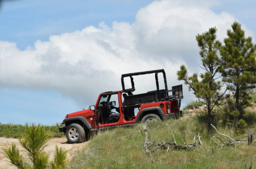 A red off-road vehicle parked on a grassy trail with blue skies and clouds in the background.